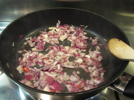 Rote Zwiebel, Knoblauch und Chilischote in Sesamöl anbraten