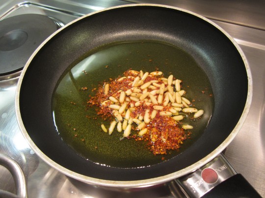 Die Pinienkerne werden mit den Chiliflocken im restlichen Olivenöl sanft geröstet, bis das Öl schön rot wird.