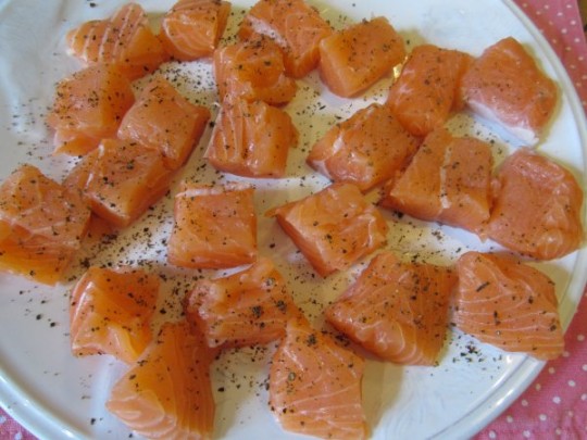 Lachs in mundgerechte Stückchen schneiden und pfeffern